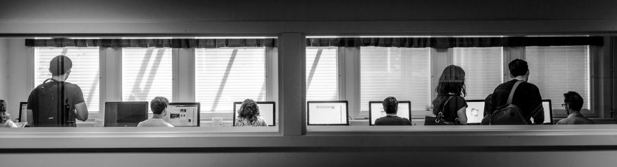 Långsmal bild som visar ett fönster in mot en datorsal där studenter sitter framför datorskärmar
